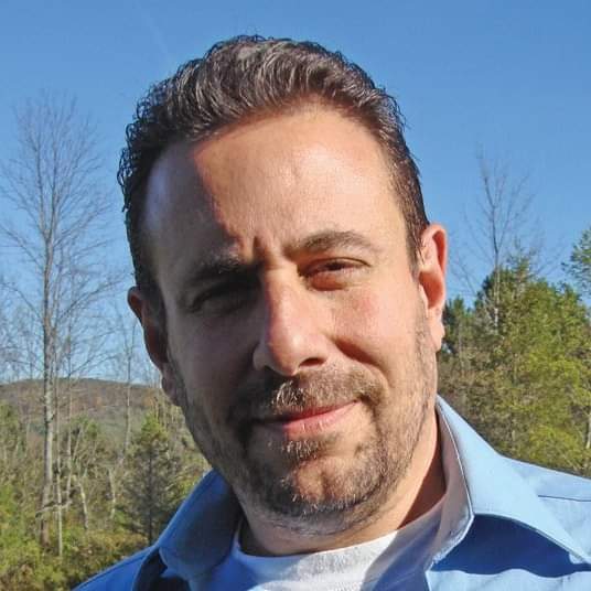 A closeup shot of a man with his head tilted. Behind him is a field.